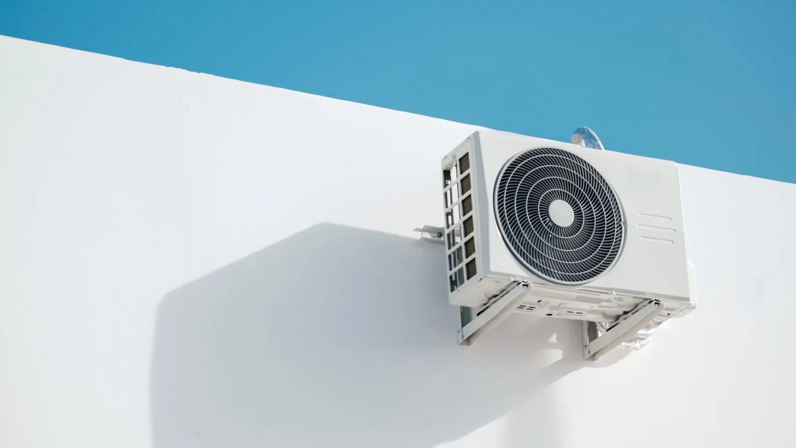 Buitenunit van een warmtepomp naast een woning; het verbruik van een warmtepomp hangt af van woning en isolatie