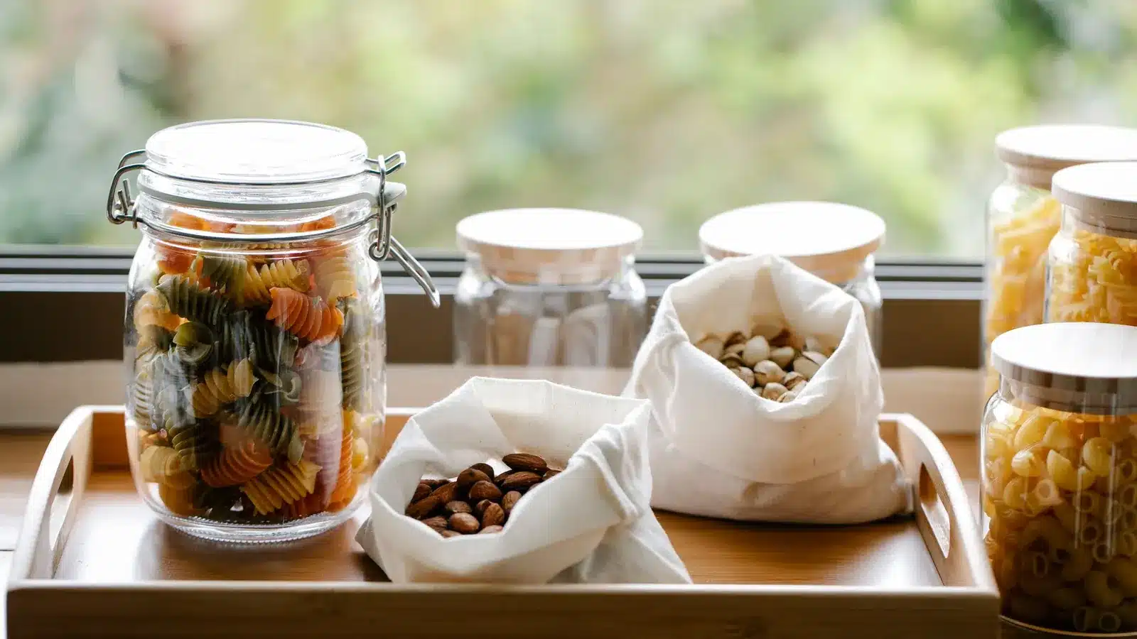 Zero waste tips in de keuken: glazen voorraadpotten, een stoffen tas en losse groente op het aanrecht